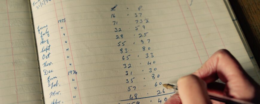 a hand holding a pen writing in an accounting book